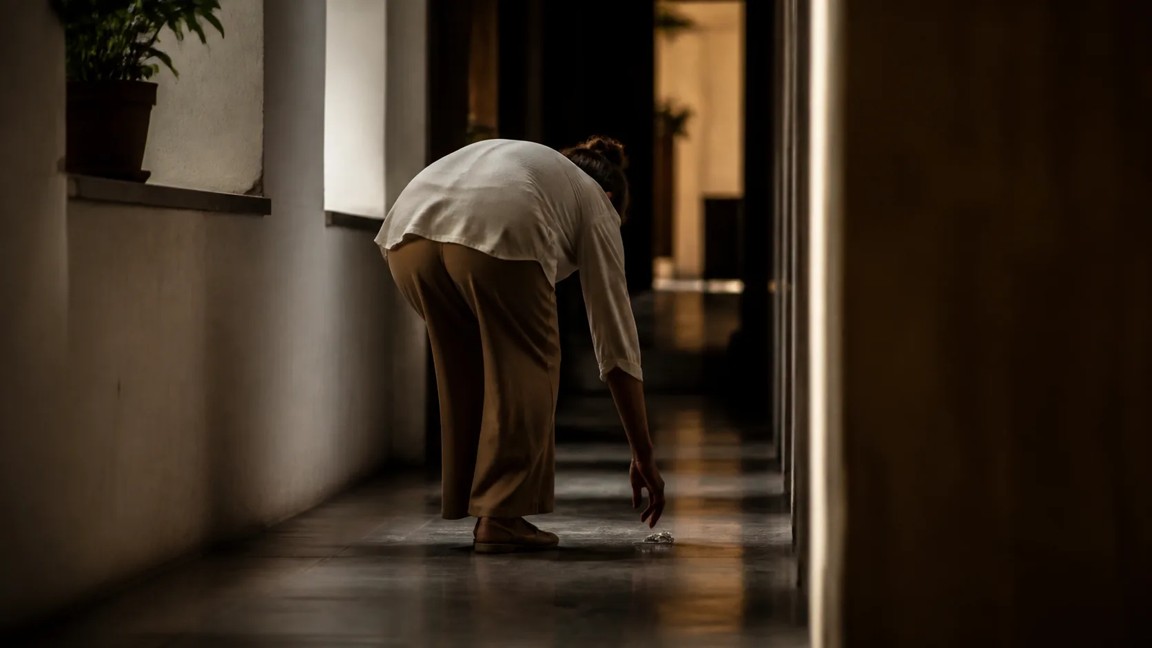 Pessoa recolhendo um objeto em corredor silencioso, representando integridade sem testemunhas.